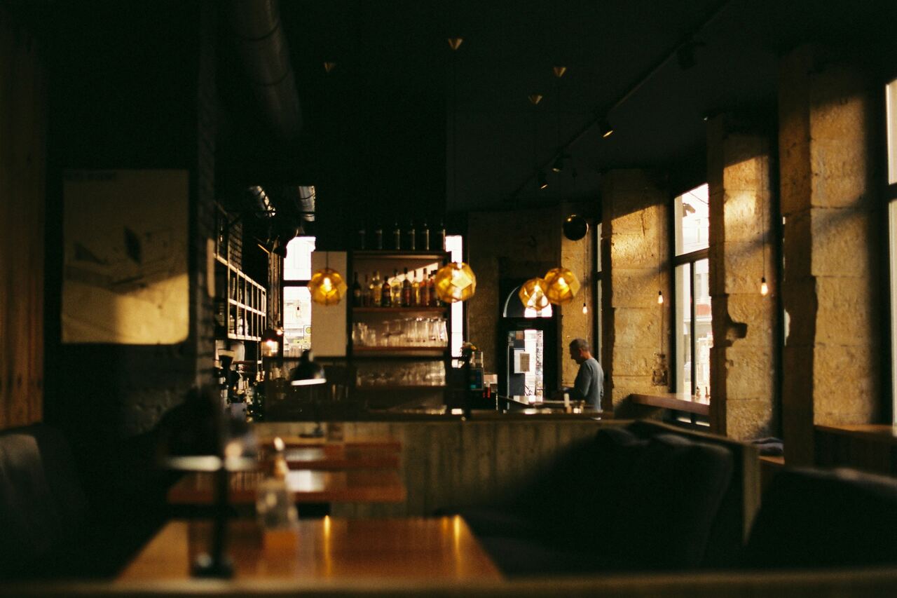 Salle de café en fin de journée, lampes ambrées et comptoir au fond.