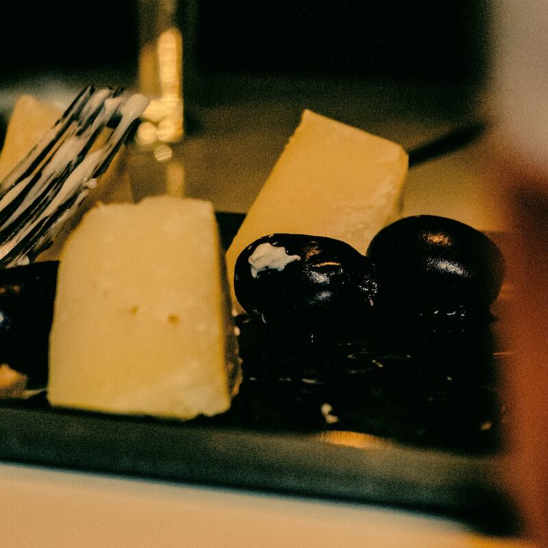 Morceaux de fromage et olives sur une planchette, verre de bière flou au premier plan.